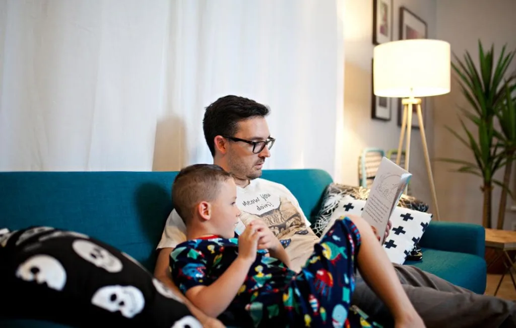 Pai calmo lendo histórias num livro para seu filho no sofá