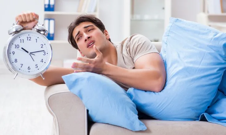 Foto ilustrativa mostra homem querendo meditar com um despertador gigante na mão