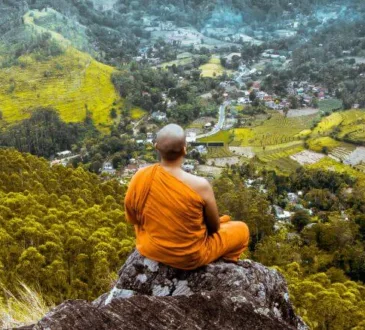 Monge de roupa laranja sentado em uma pedra na montanha olhando o vilarejo lá embaixo