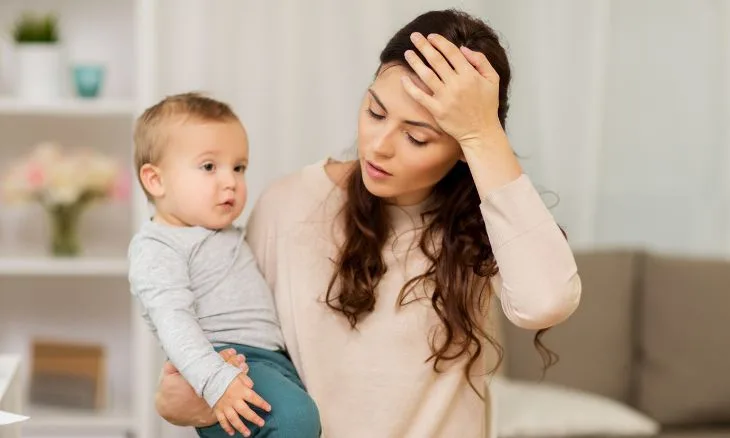 Mãe com criança no colo e mão na testa