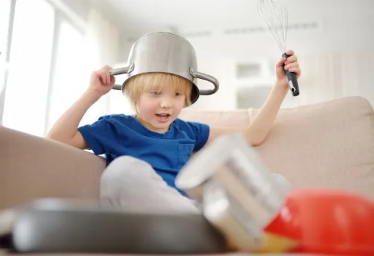 Menino com uma panela na cabeça brincando e fazendo barulho