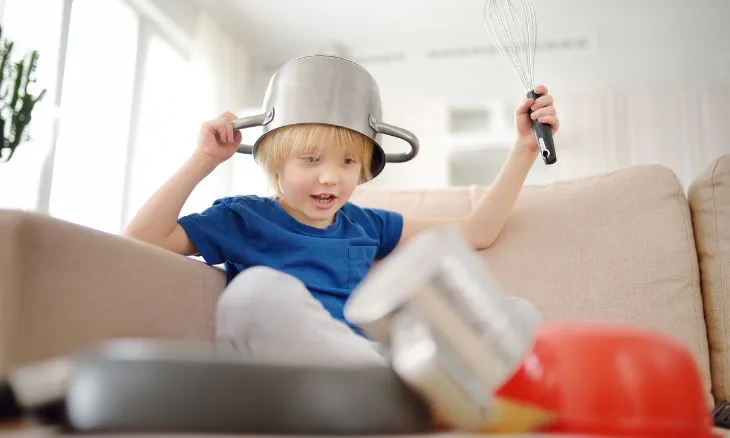 Menino com uma panela na cabeça brincando e fazendo barulho