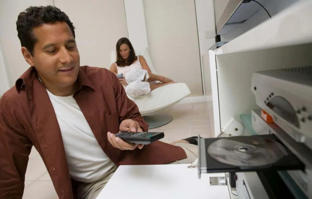 Homem colocando um dvd no DVDPlayer na sala