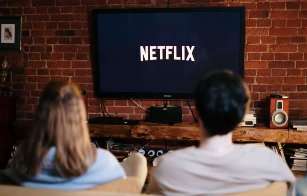 Casal sentado na sala, na tela da tv a palavra Netflix