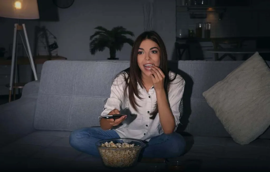Mulher empolgada comendo pipoca e assistindo Netflix na tv da sala